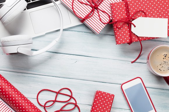 Wrapped presents, a laptop, a set of headphones, a smartphone, and a cup of coffee sitting on a table