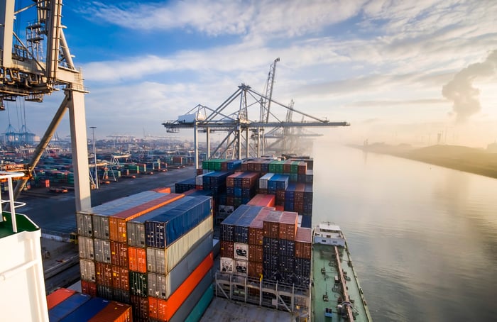 Shipping containers on a ship at port with the sun rising in the background.