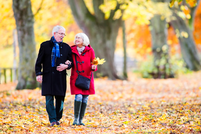 Senior couple walking in the woods with leaves on the ground in the fall