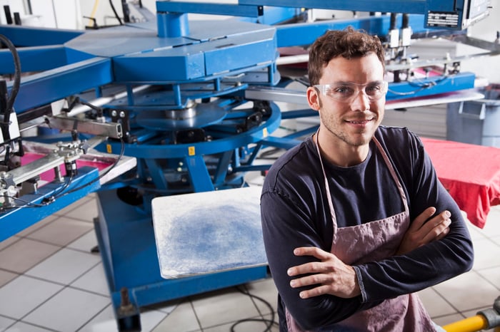 A manufacturing worker standing with his arms crossed in front of heavy-duty machinery.
