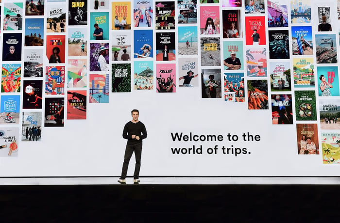 AirBnB chief executive Brian Chesky speaks onstage in front of a backdrop of different trips around the world