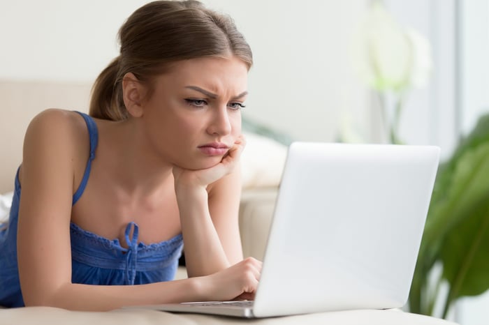 Young woman looking at her laptop while frowning and furrowing her brow. 