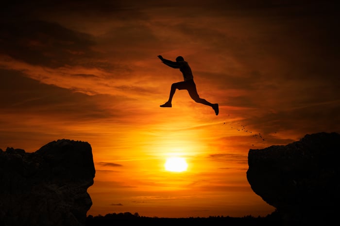 Silhouette of a man jumping over an abyss at sunset.