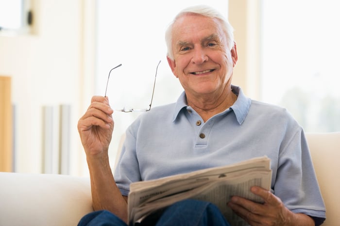 Smiling senior male holding glasses and a newspaper