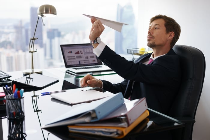 Man in suit launching a paper airplane at his desk