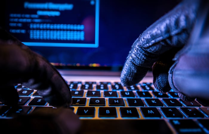 A computer hacker wearing black gloves typing on a keyboard. 