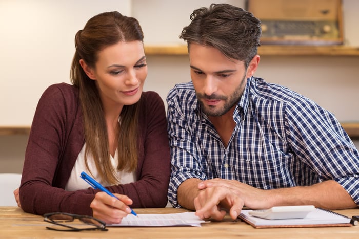 Woman writing on a piece of paper next to a man with a calculator