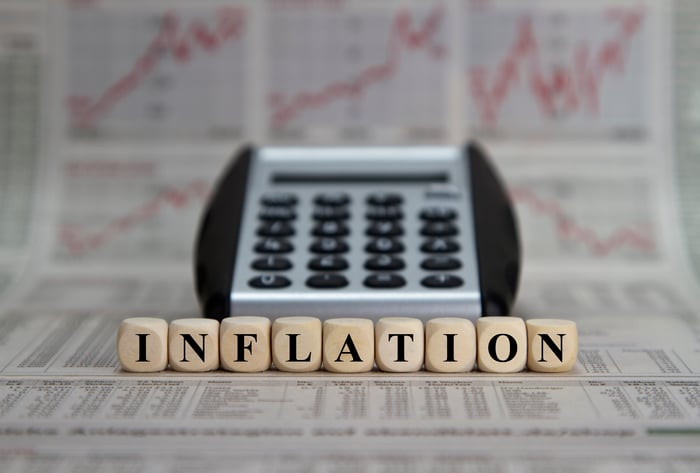 Dice spelling out the word inflation in front of a calculator, with rising charts in the background. 