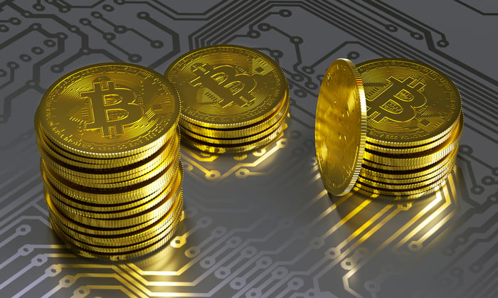 Physical gold bitcoin stacks lying atop a gray circuit board. 