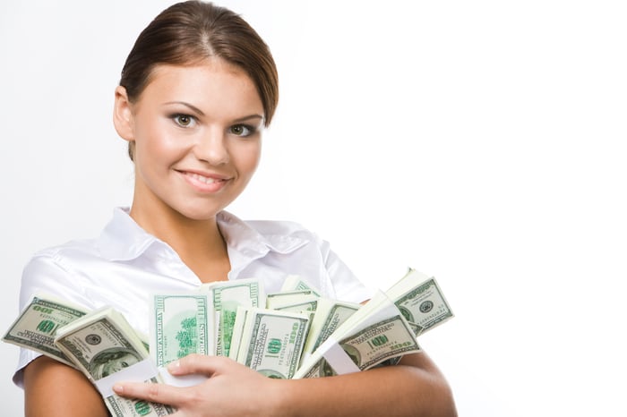 A young smiling woman holding stacks of cash in her arms. 