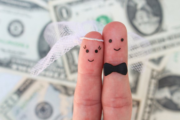 two fingers being held up against background of cash -- they're drawn on so that one, wearing a veil, represents a bride and the other, in a bow tie, represents a groom