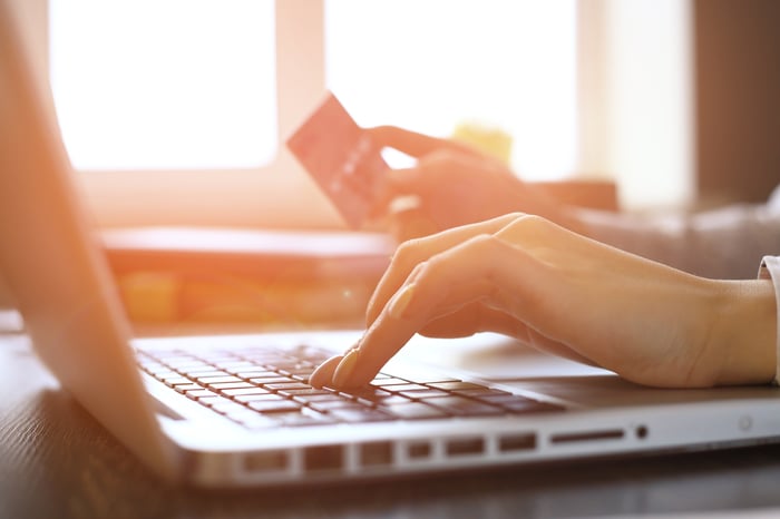 A woman's hand hovers over a keyboard while the other holds credit card.