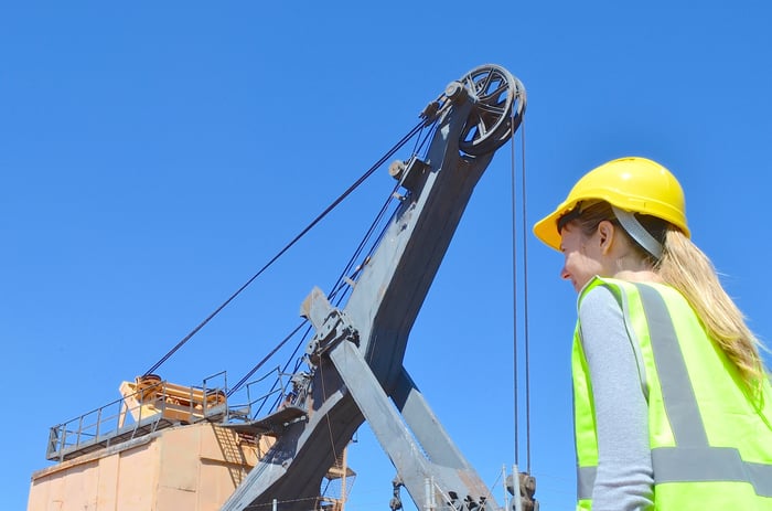 A woman in a hard hat and reflective vest standing in front of mining equipment