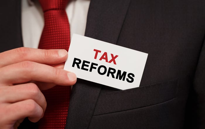 A man in a suit putting a business card that says tax reforms in his front pocket. 