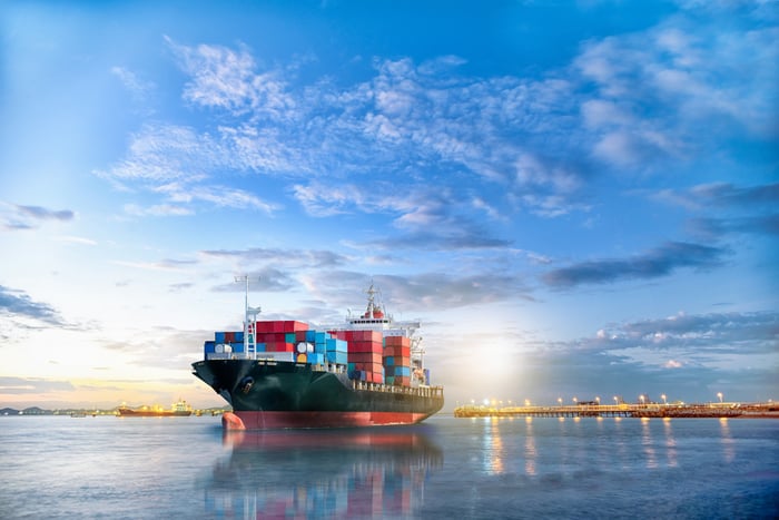 A containership reflecting on the water with the sun in the background.