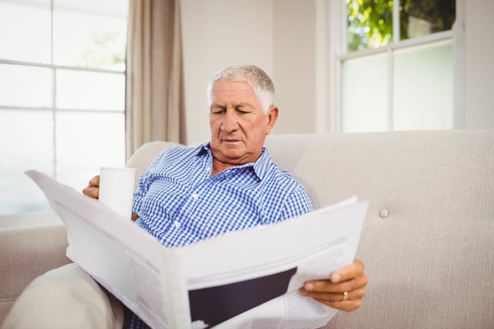 Senior male reading the newspaper with mug in hand