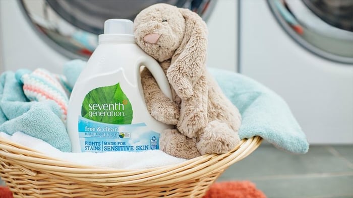 Plush dog toy with arm wrapped around a bottle of Unilever's "Seventh Generation" brand laundry detergent in laundromat.