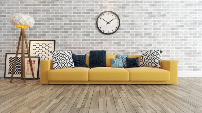 Living room with wood flooring, couch, and a large wall clock on a gray brick wall