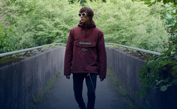 Young man on forest bridge with dark sunglasses wearing a Napapijri brand jacket.