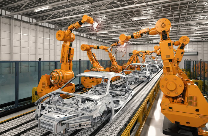 Robotic arms working along both sides of an auto assembly line, with several car frames on it.