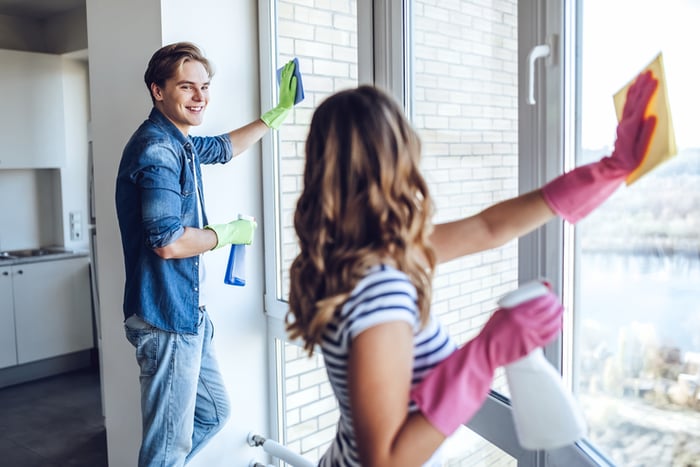 Young couple cleaning windows in apartment with household cleaning products.