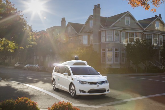 A Chrysler Pacifica minivan outfitted with Waymo self-driving technology on a sunny street.