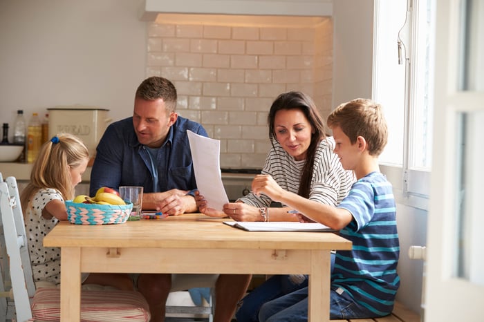 Two adults and two children sitting and talking at a kitchen table.