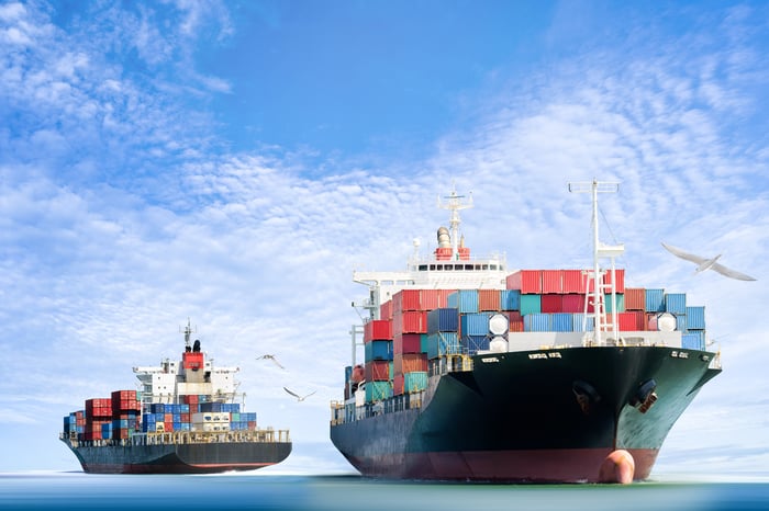 Container ships in the water with birds flying by under a blue sky.