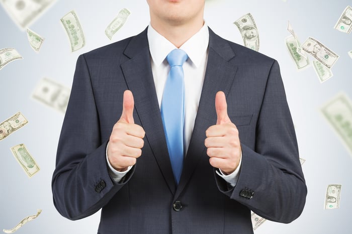 Man in suit making a thumbs-up gesture with money in background