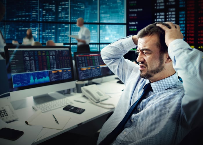 A frustrated stock trader grabbing his head and looking at losses on his computer screen.