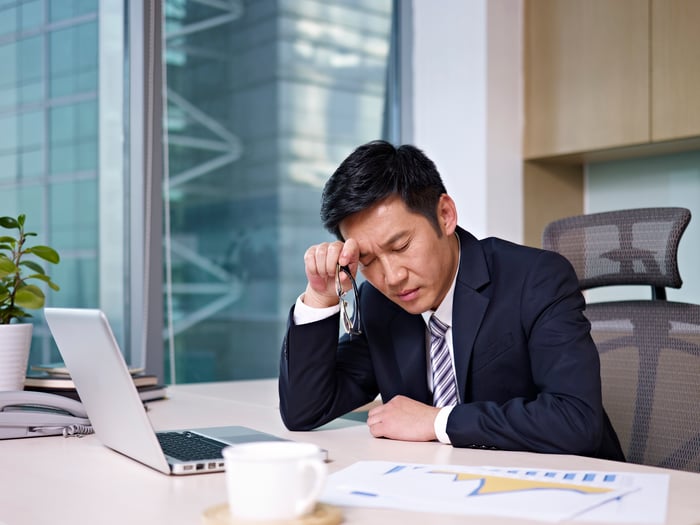 Man in suit holding his head at his desk