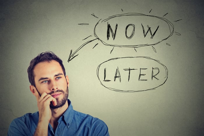 Man looking thoughtful in front of a board with options "Now" and "Later"