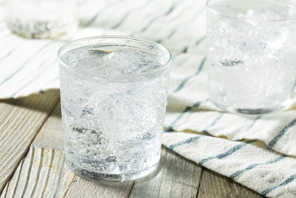 Sparkling water with ice cubes in a glass on a wood-slat table.