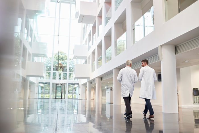 Two people in lab coats talking as they walk through the lobby of a building.