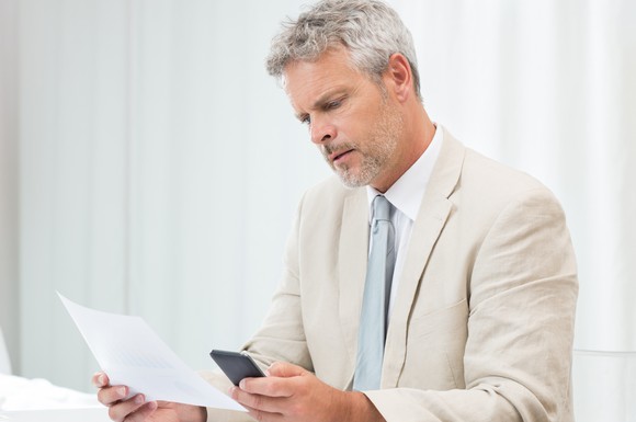 Senior man in a suit looking at a phone and a document