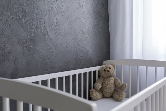 Stuffed bear sitting in the corner of a baby crib.