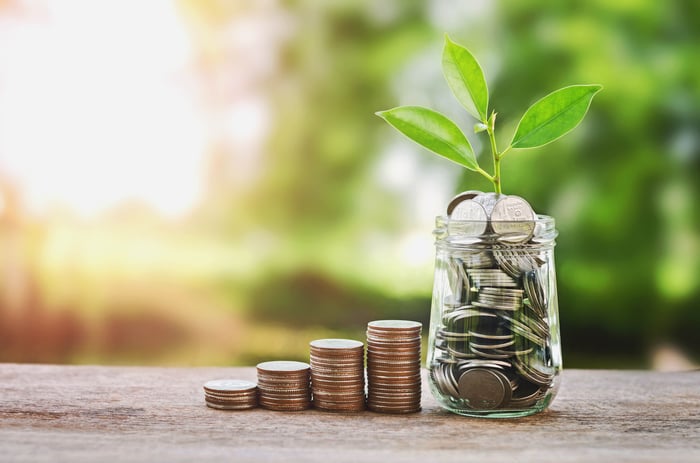 Growing stacks of coins leading to plant growing out of glass coin jar.