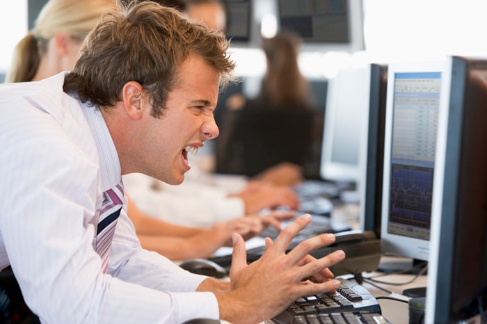 Frustrated person in front of computer monitors and keyboard.