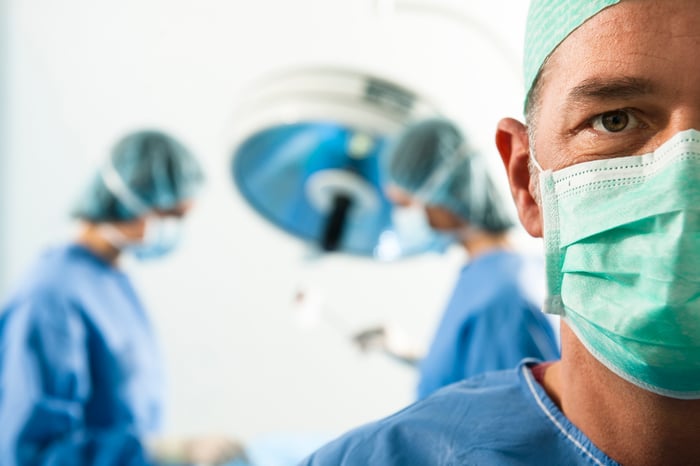 A surgeon in the foreground with an operation happening in background.