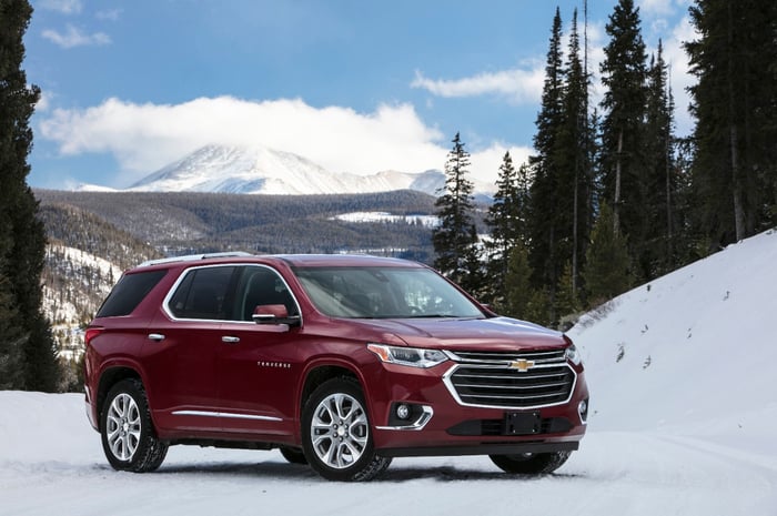 A red Chevy Traverse parked on snow, with tall trees in the background