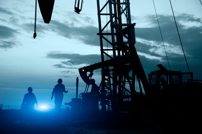 Silhouette of workers and an oil drill rig.