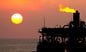 Gas flaring off an offshore oil platform with the sun in the background.