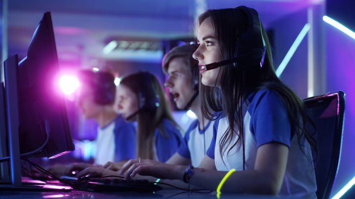 Girl in darkened room with headset playing with other players in video game competition.