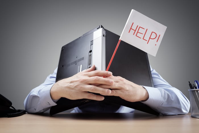 Man burying his head in an open laptop while holding a help sign