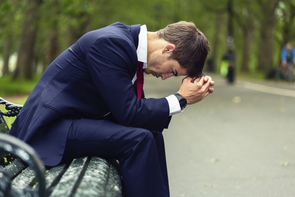 Man in suit on a park bench with his head down