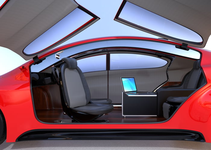 A parked red car with the wing doors raised showing an interior comprised only of seats and a table with a laptop sitting on it