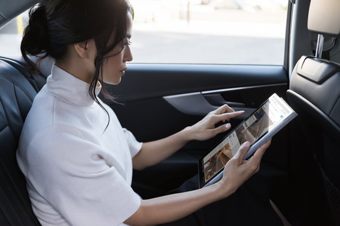A woman holding a Surface Pro in the back of a car.