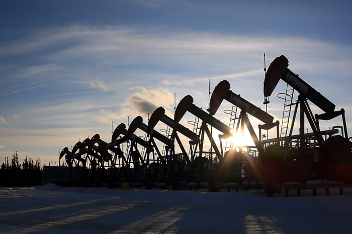 A long row of pumpjacks under the setting sun, with snow in the foreground