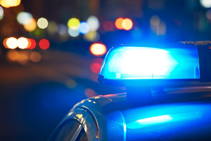 Top view of a police car traveling on a city street at night, which shows its flashing blue light. 