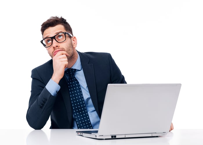 Man in suit daydreaming at a laptop.